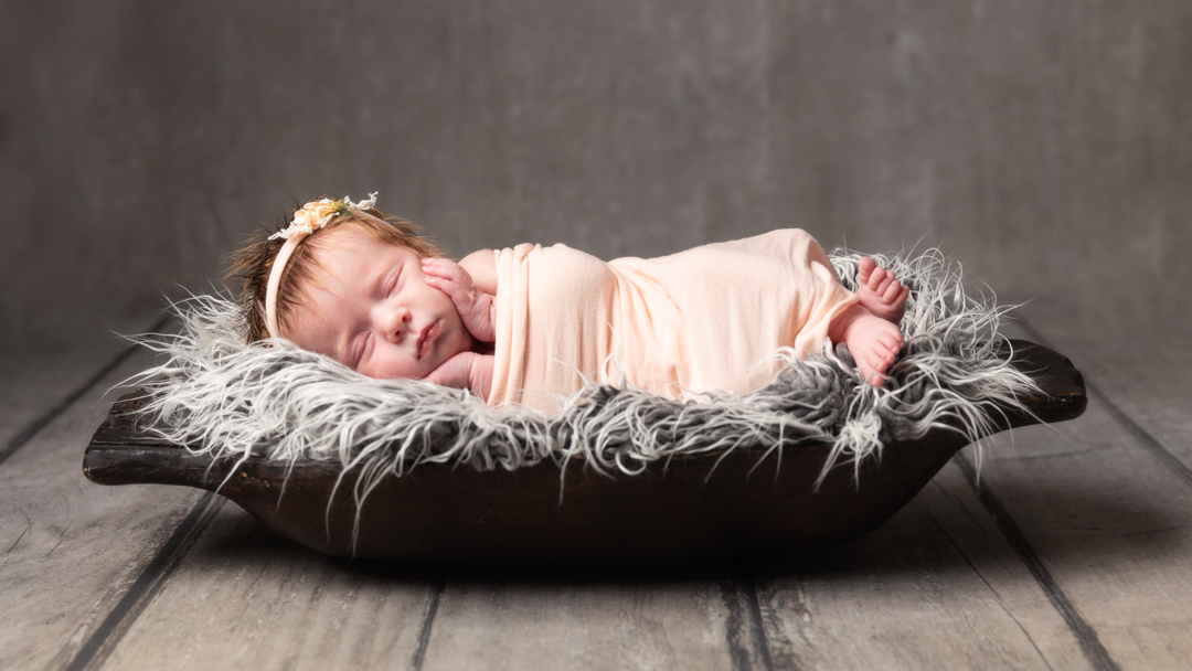 Newborn baby girl asleep in bowl on grey background