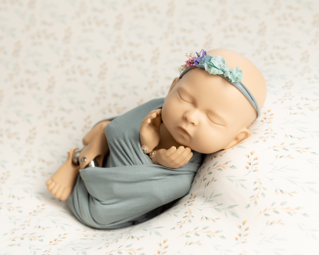 newborn doll wrapped in teal on flowery backdrop