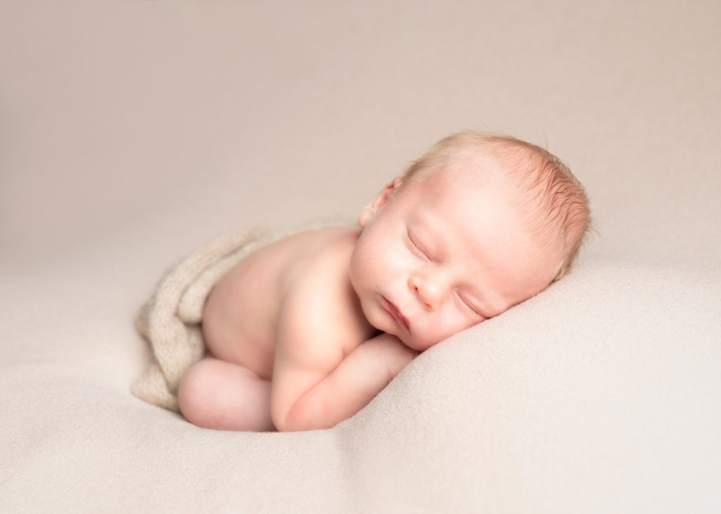 baby asleep on a cream blanket covered with cream wrap posed for newborn photograph 