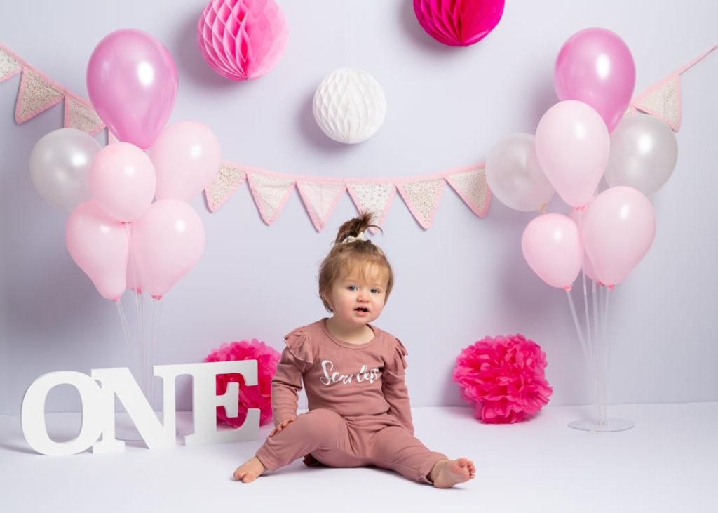 Girl celebrating her first birthday with a white ONE sing balloons and bunting