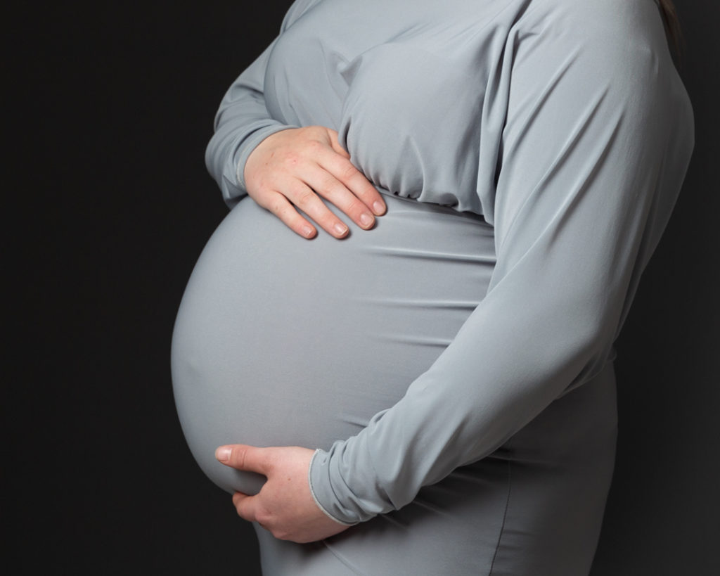 Pregnant lady wearing grey dress holding her bump