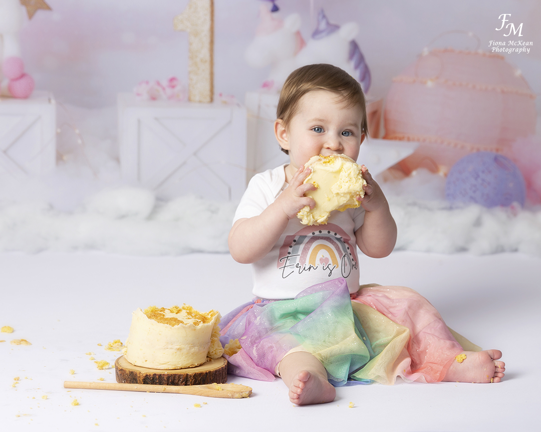 1 year old girl in rainbow outfit eating cake