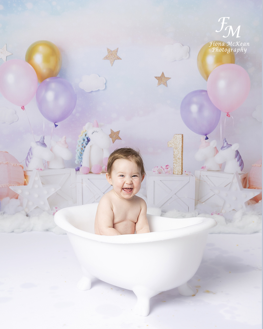 1 year old girl in bath with a unicorn themed backdrop
