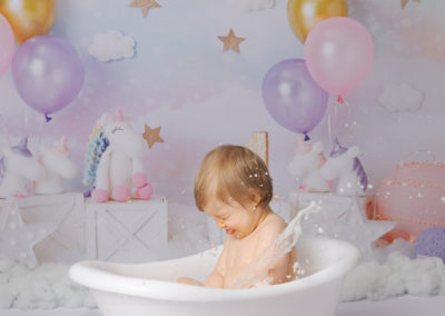 Little girl in a small bath splashing during her first birthday photoshoot