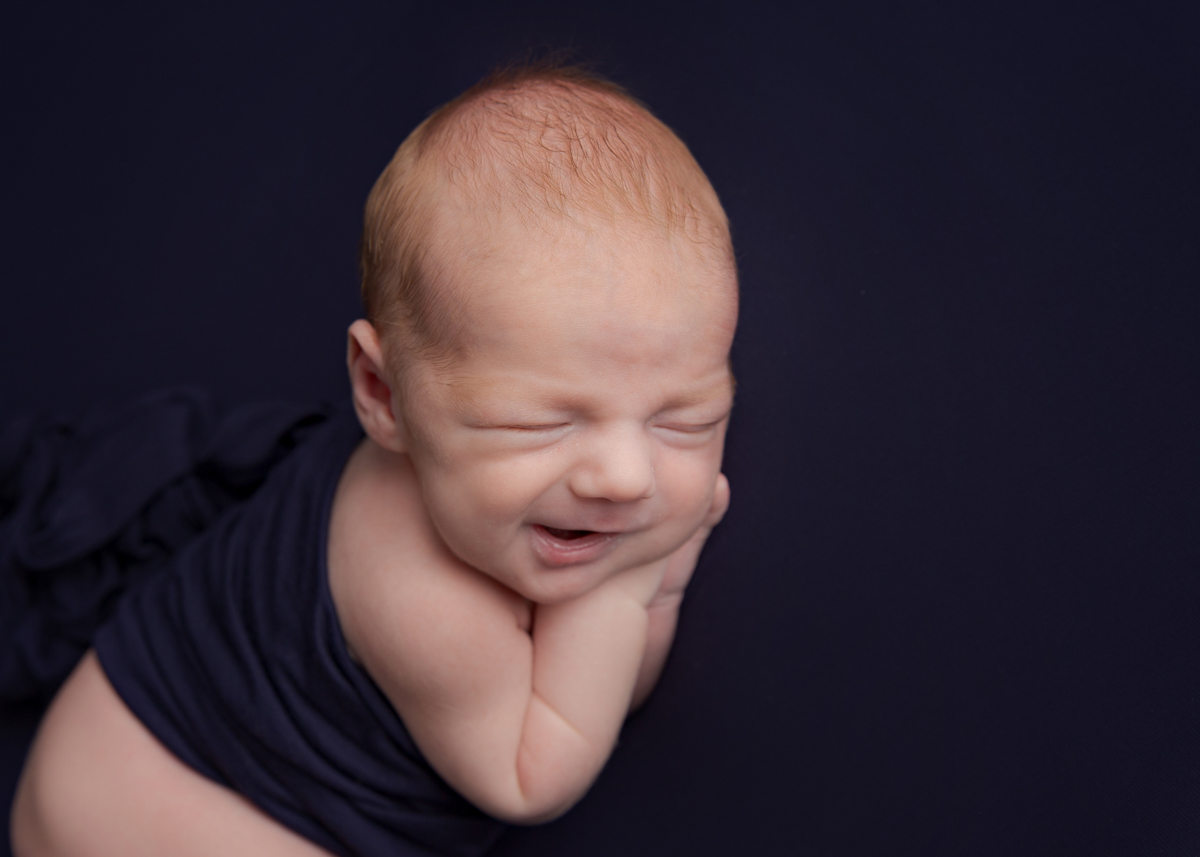 Newborn Baby boy sound asleep giving the photographer a 'windy' smile during his first photoshoot