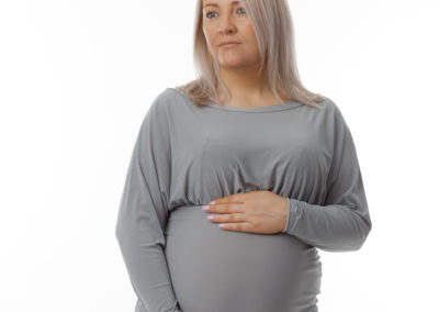 Pregnant lady with a pensive expression wearing a grey maternity dress